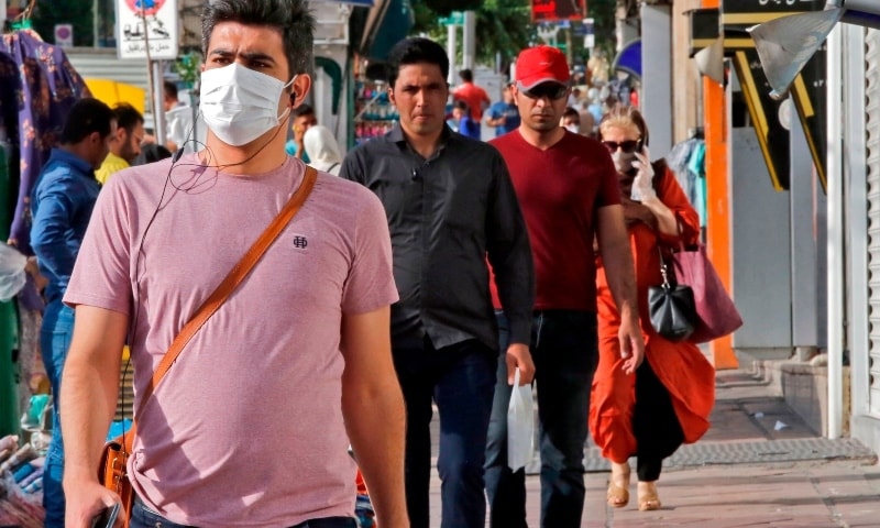 Iranians, some wearing face masks, walk along a street in Tehran on June 3. — AFP