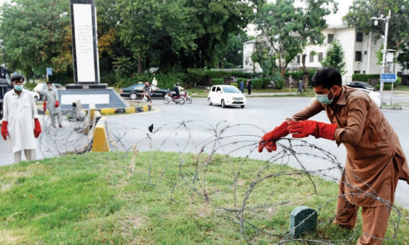 A district administration official places a barbed wire at Shuhada Chowk near Melody Market to seal off G-6 on Wednesday. Several localities in Islamabad were locked down after an increase in the number of positive cases were reported in the areas. &mdash; Photo by Mohammad Asim