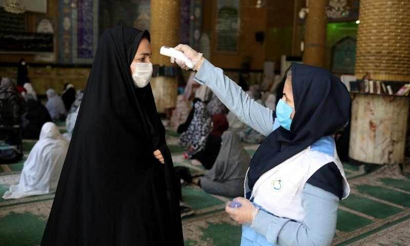 In this file photo, an Iranian woman wearing a protective face mask checks the temperature of a worshipper before attending the Friday prayers in Qarchak Jamee Mosque. &mdash; Reuters