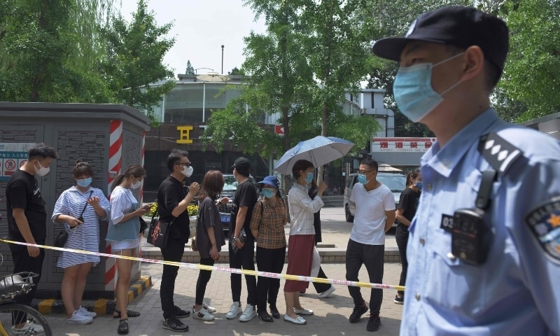 A policeman keeps watch as people wait in line to undergo Covid-19 tests at a testing station in Beijing on June 28. — AFP
