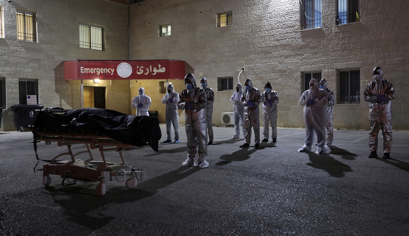 Health workers and people in protective suits pray before the body of a Palestinian woman who has died after contracting Covid-19, in Nablus, in the Israeli-occupied West Bank on July 5, 2020. &mdash; Reuters