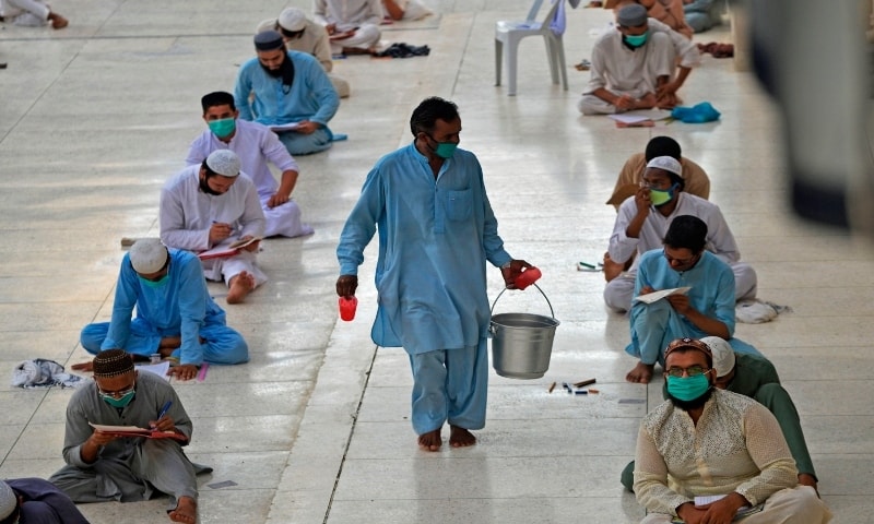 A helper carries drinking water as students wearing facemasks as a preventive measure against the spread of the Covid-19, attend their final examination at Jamia Binoria seminary in Karachi on July 13, 2020. &mdash; AFP