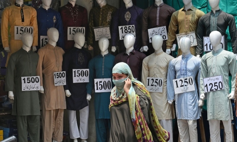 A woman walks past mannequins kept on display outside a cloth shop at a market in Lahore on July 27.  — AFP