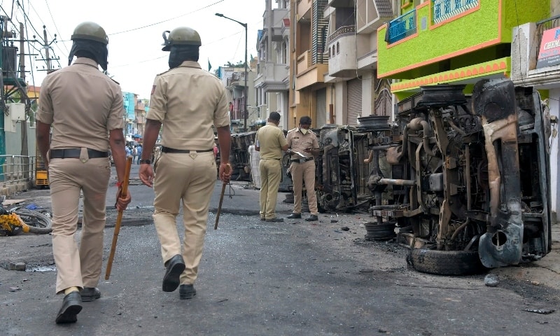 Policemen stand guard next to burnt police vehicles along a street in Bangalore on August 12. — AFP