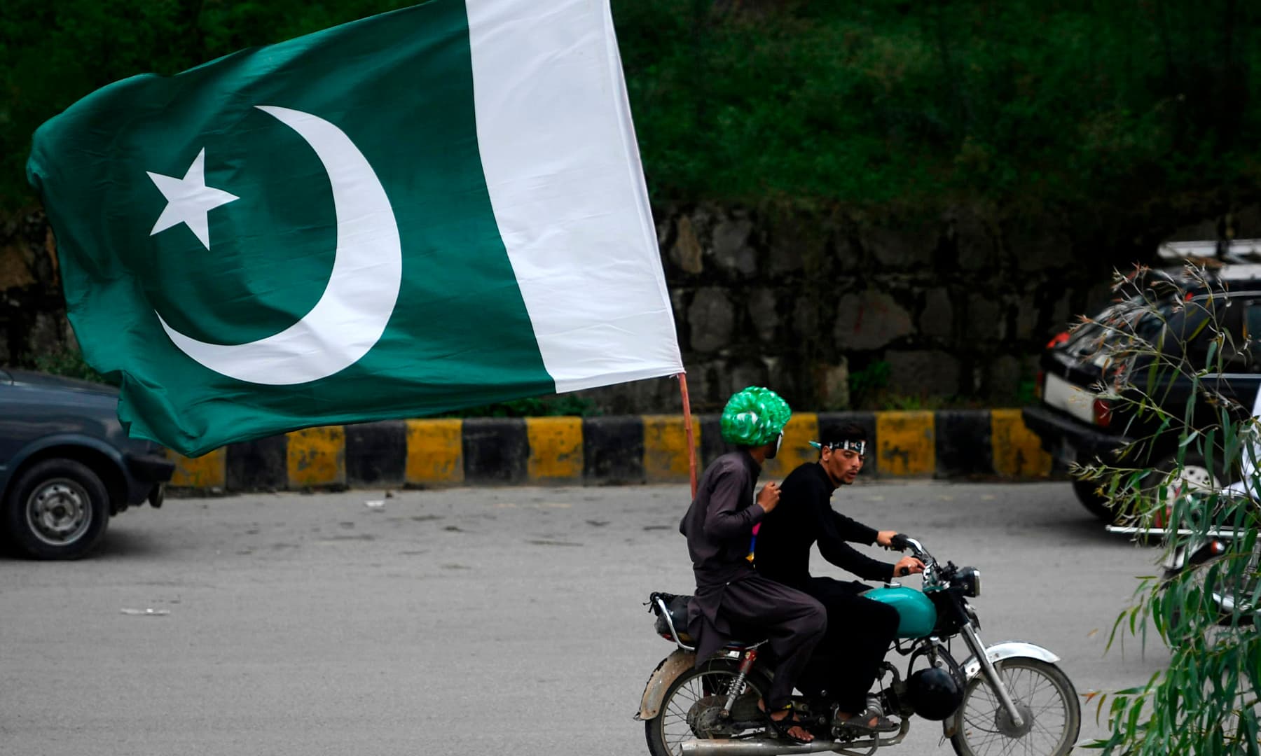 Men ride on a bike with a large flag of Pakistan along a street during Independence Day celebrations in Islamabad on August 14. — AFP