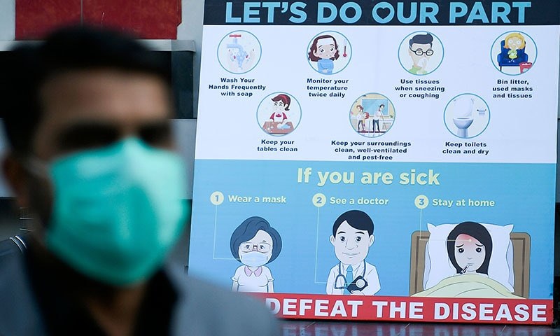 A man wearing a facemask walks past a sign board displaying preventive measures against the spread of the Covid-19 outside a mall in Islamabad on March 16, 2020. — AFP/File