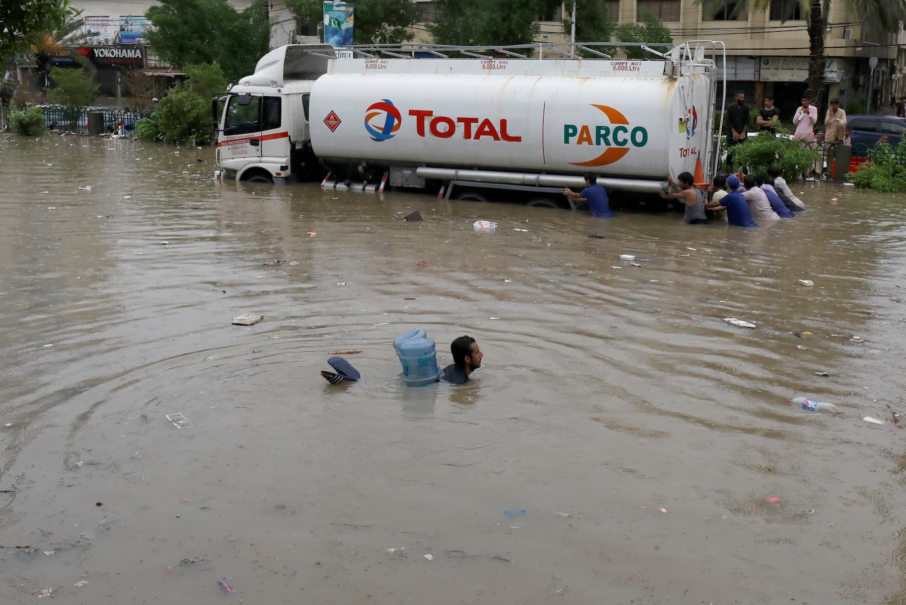 A man swims with the help of empty canisters through a flooded road in Karachi during the monsoon rain on Tuesday, August 25. — Reuters