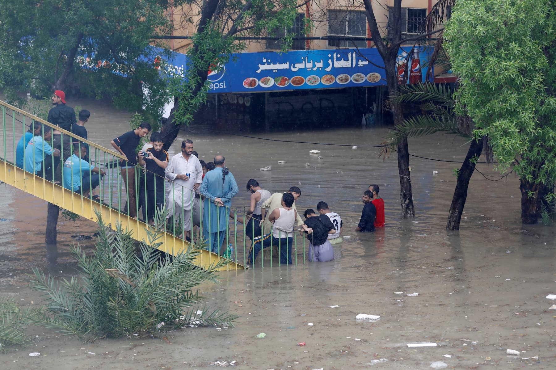 People gather on the stairs of a pedestrian bridge on a flooded road during the downpour in Karachi on Tuesday, August 25. — Reuters