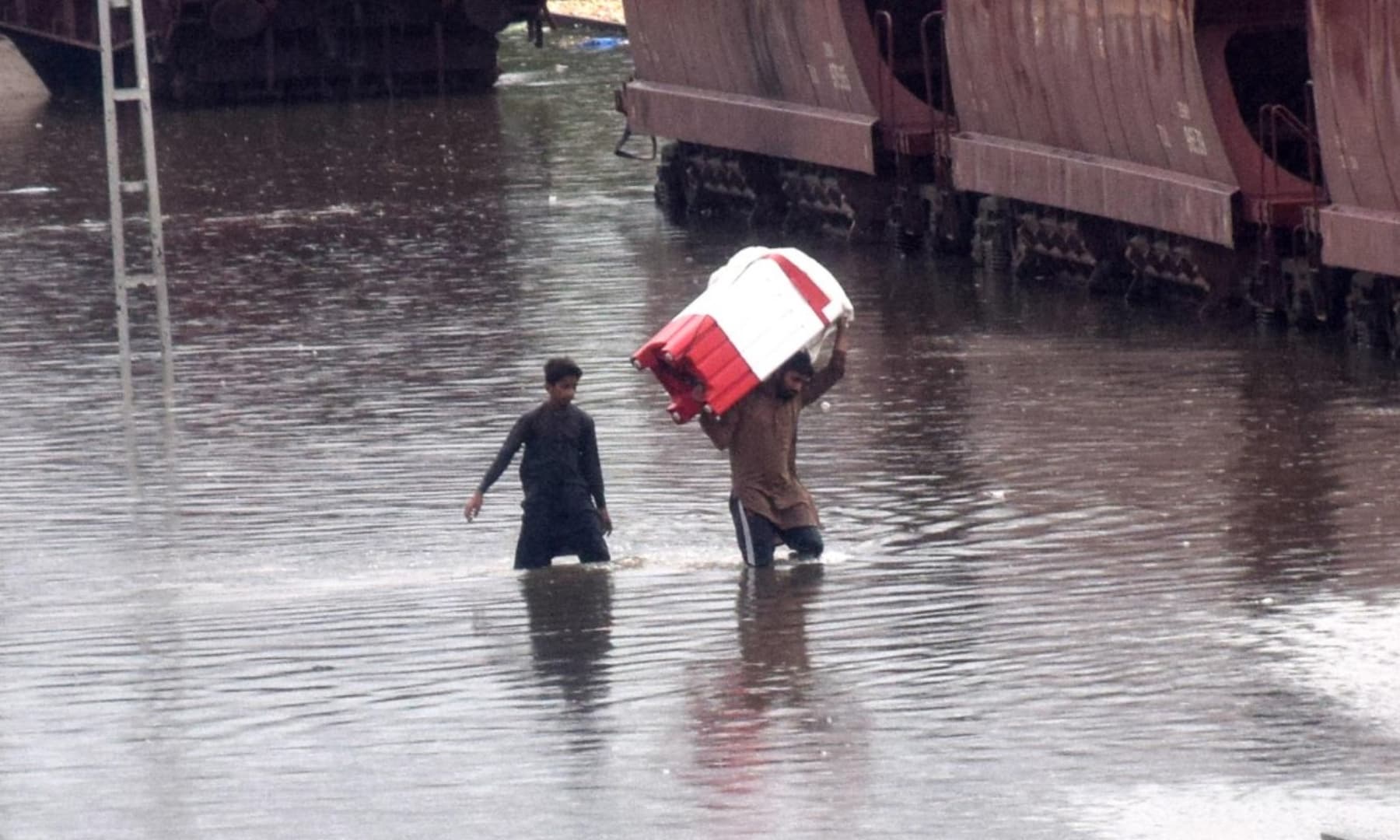 A man carries a washing machine on his shoulder to pass through Hyderabad railway station where tracks were completely submerged after Monday and Tuesday's rainfall. — Umair Ali