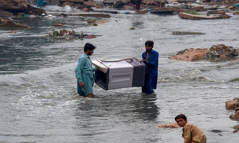 People carry a washing machine through a flooded residential area after heavy monsoon rains in Karachi on August 27, 2020. — AFP