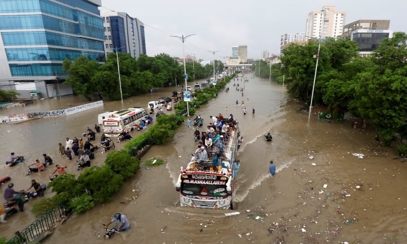 People sit atop a bus roof while others wade through a flooded road during monsoon rain in Karachi on August 27, 2020. — Reuters