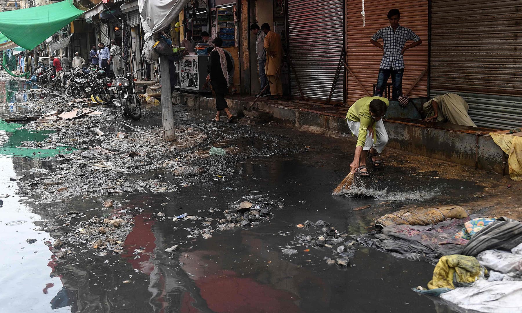 A man cleans in front of shops after a street flooded following heavy monsoon rains in Karachi on August 31. — AFP