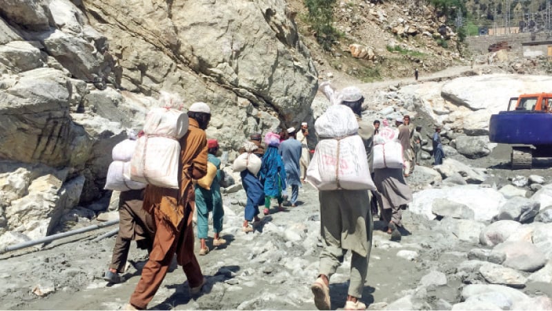 People carry food supplies to their homes in Dubair Kohistan after road was washed away by flash floods. — Dawn