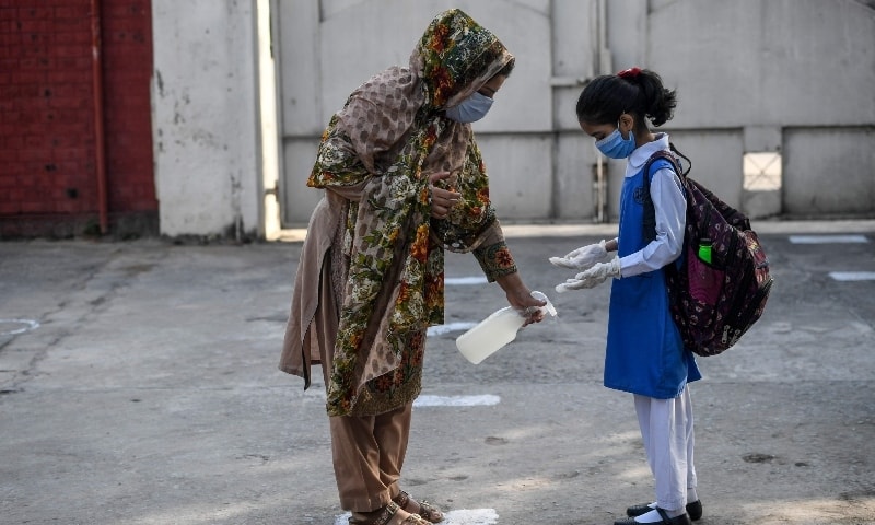 A teacher (L) sprays disinfectant on the shoes of a child wearing a facemask and gloves at the entrance of a junior campus school upon arrival in Islamabad on September 30. &mdash; AFP
