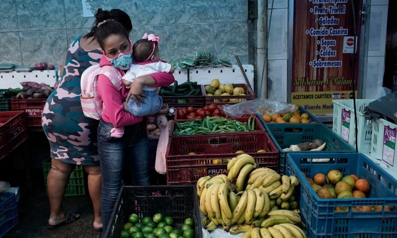 A woman carrying a baby buys fruit at a shop in Rio de Janeiro on October 9. — AP
