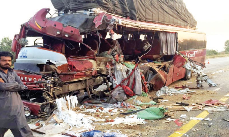 A man walks past the damaged passenger bus after an accident with a dumper truck on the motorway in Swabi on Wednesday. — Dawn