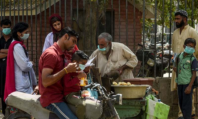 Customers wearing facemasks as a prevention measure against the COVID-19 coronavirus buy corn from a street vendor (C) along a street in Karachi on March 10. — AFP/File