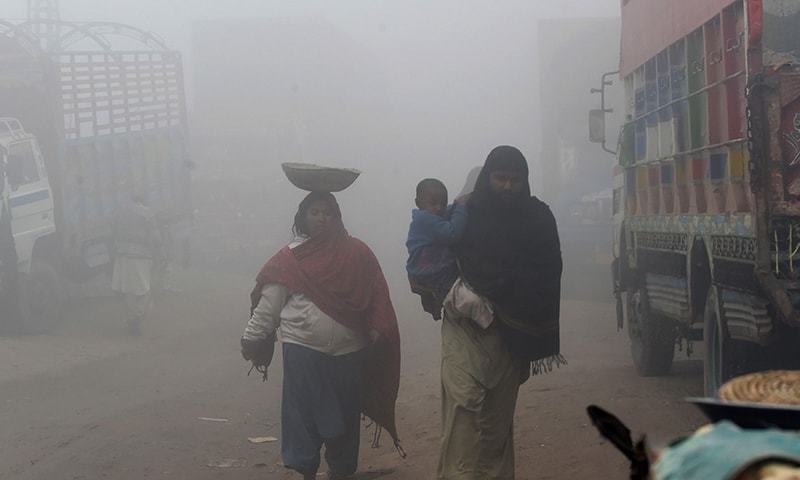 A Pakistani family walk during dense fog and smog in Lahore on December 24, 2018. — AFP/File