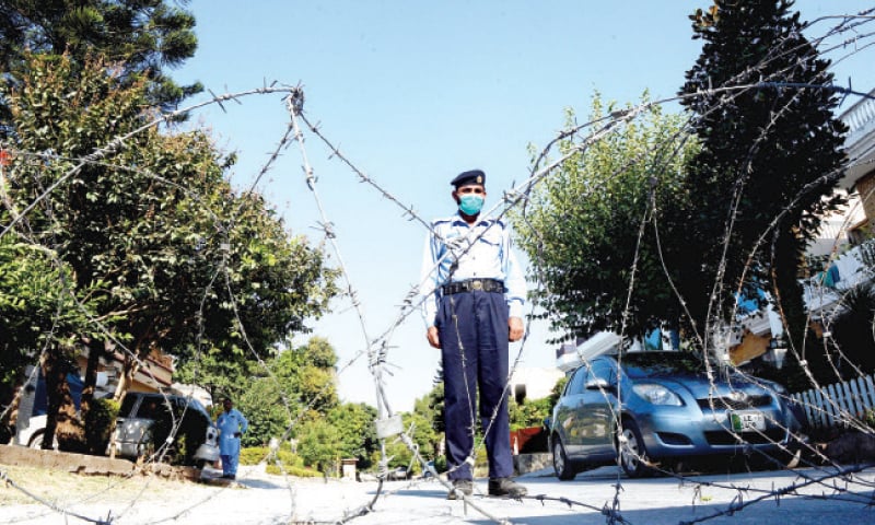 A policeman stands near barbed wire placed on a street in I-8/4 after Covid-19 cases were reported in the area on Monday. &mdash; Photo by Mohammad Asim