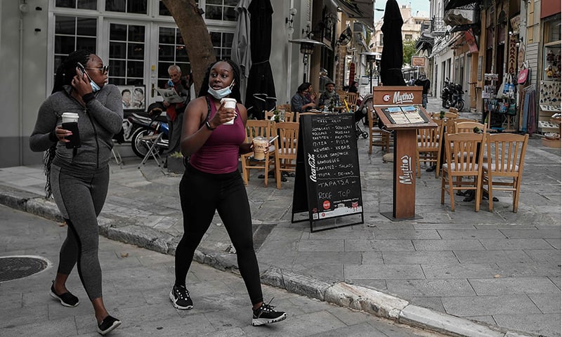 Tourists walk past a cafe with take away signs a day before their closure on November 2 in Greece. — AFP