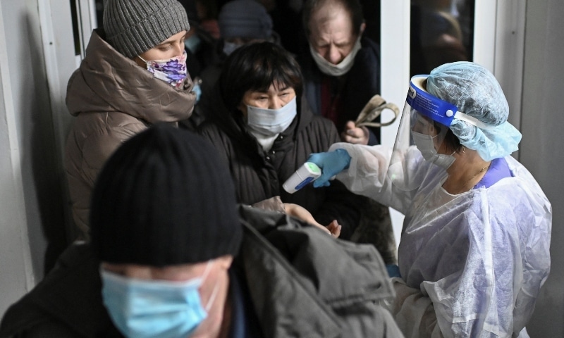 People wearing protective face masks have their body temperature checked at an entrance to a local clinic in Omsk on November 9. — Reuters
