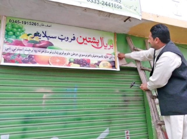 A man fixes a board in Pashto language at a shop in Peshawar. — Dawn