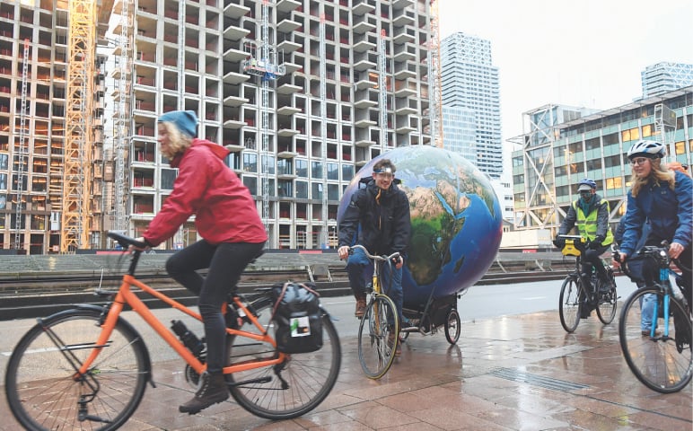 The Hague (Netherlands): People ride their bikes as environmental activists protest outside a court on Tuesday during a hearing in a case environmentalists and human rights groups have brought on against Royal Dutch Shell to force the firm to cut its reliance on fossil fuels.—Reuters