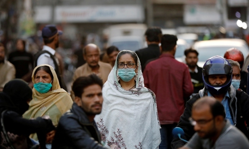 Women wear protective masks as they walk through a crowd along a market in Karachi on Dec 2. —  Reuters