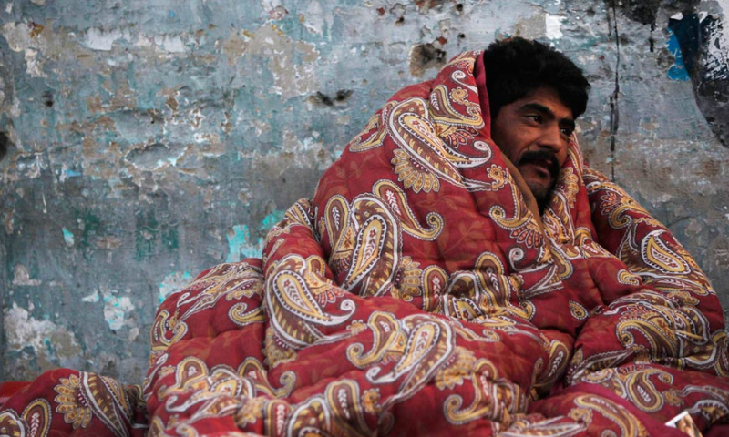 A man covers himself with a cotton blanket to stay warm during winter in the early hours of the morning near a bus stop in Karachi. &mdash; Reuters/File