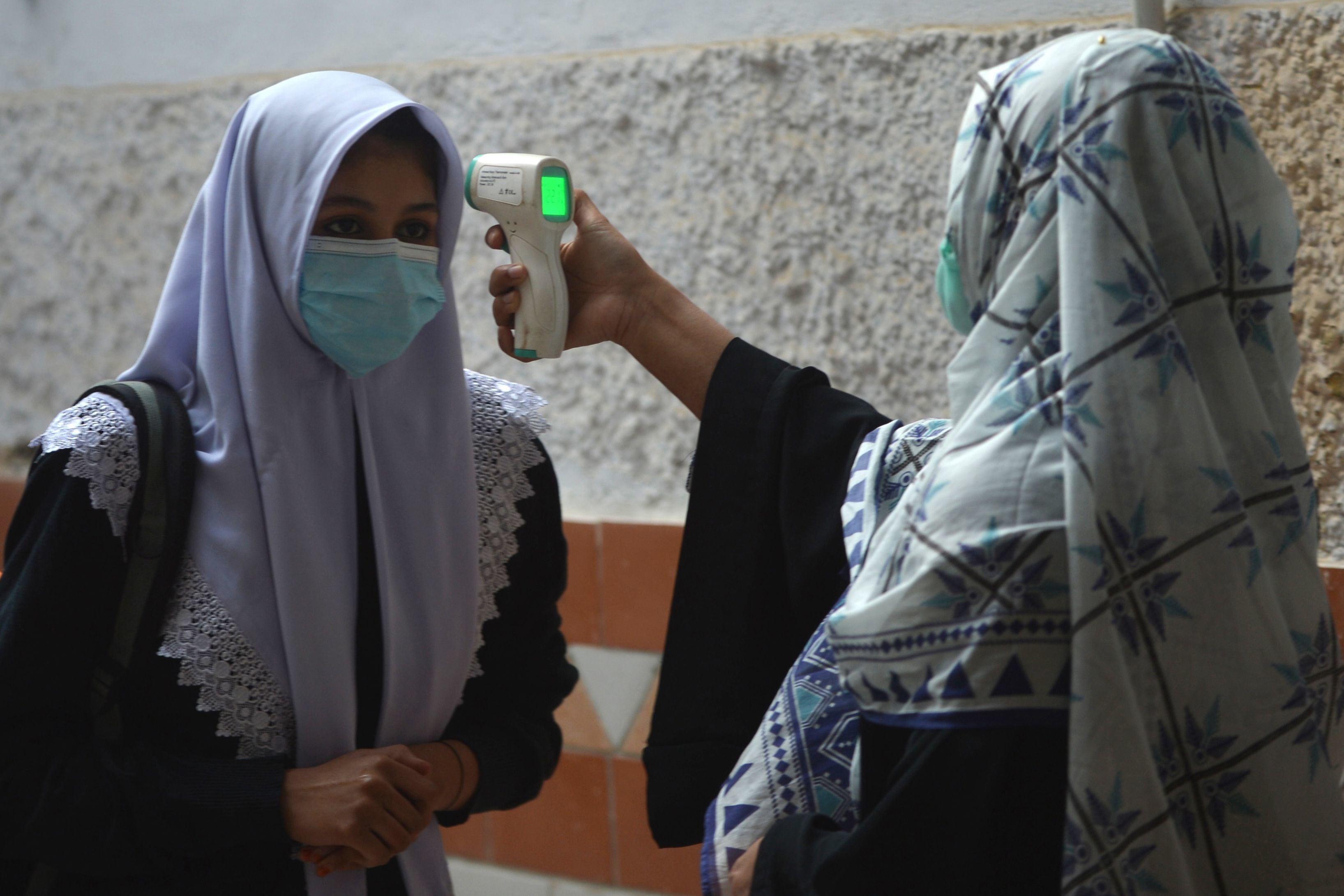 A teacher (R) checks the body temperature of a student wearing a facemask upon her arrival at the school in Karachi on January 18. — AFP