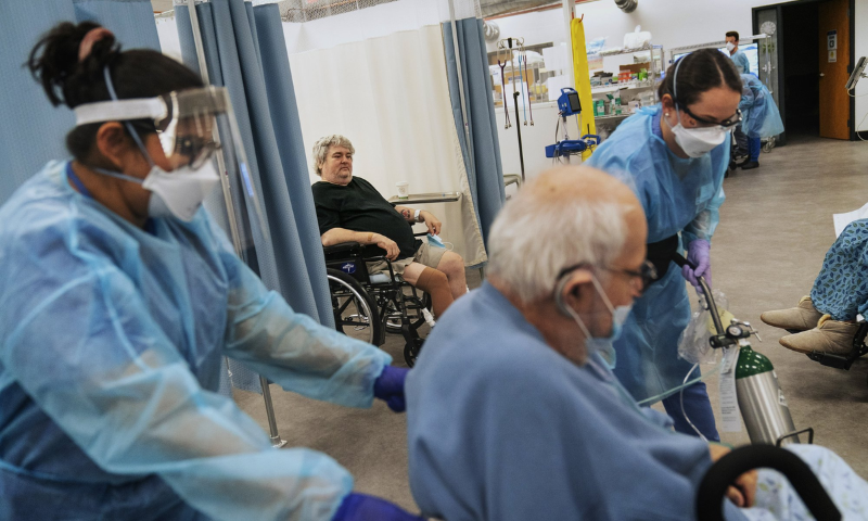 Covid-19 patient Art Singleton, 56, rear, watches as fellow patient Nicholas DiPompo, 78, is wheeled to the exit by registered nurses, Doris McClellan, left, and Ashley Nowlin, right, for discharge from a field hospital in Cranston, R.I, on January 6, 2021. — AP