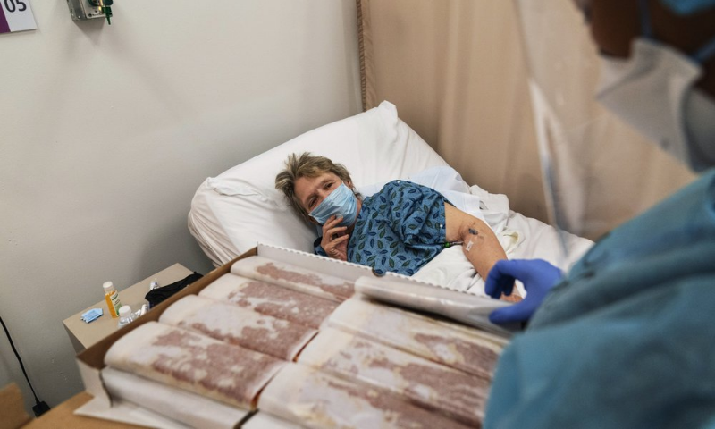 Covid-19 patient Linda Cotrone, 72, of Warwick, R.I., is offered a slice of pizza by certified nephrology nurse Scarlett Santana, after a fellow patient bought pizza for the staff on December 14, 2020. — AP