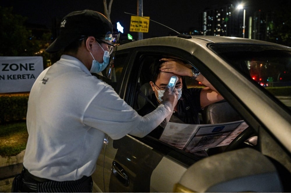 This picture taken on February 9, 2021 shows a waiter checking the temperature of a customer before taking his order for the “dine in car” service outside the Padi House restaurant in Cyberjaya, outside Kuala Lumpur. — AFP