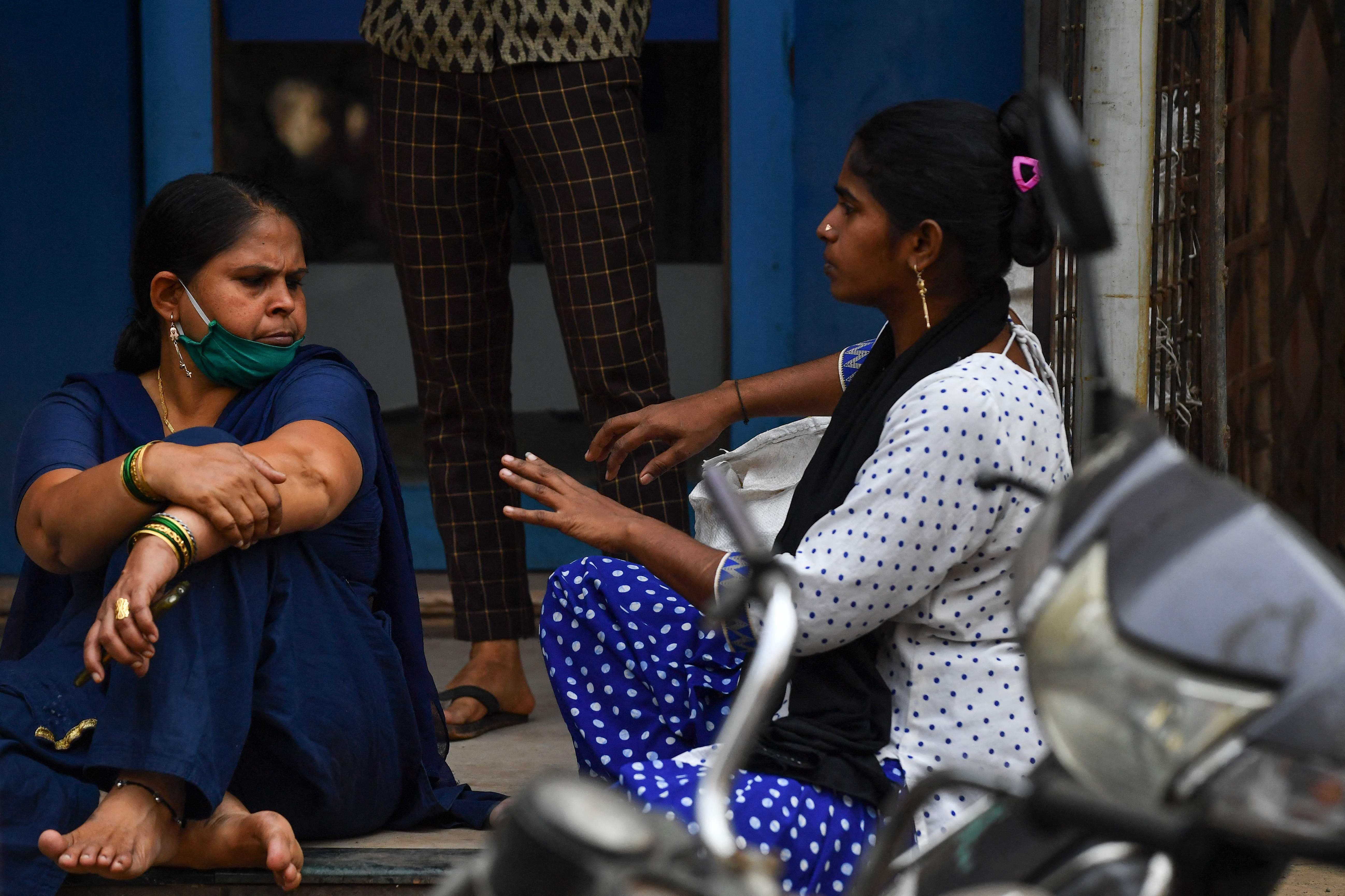 A woman (R) chats without wearing a face mask despite restrictions imposed as a preventive measure against the spread of the Covid-19 coronavirus, at Dharavi slum in Mumbai on February 23. — AFP