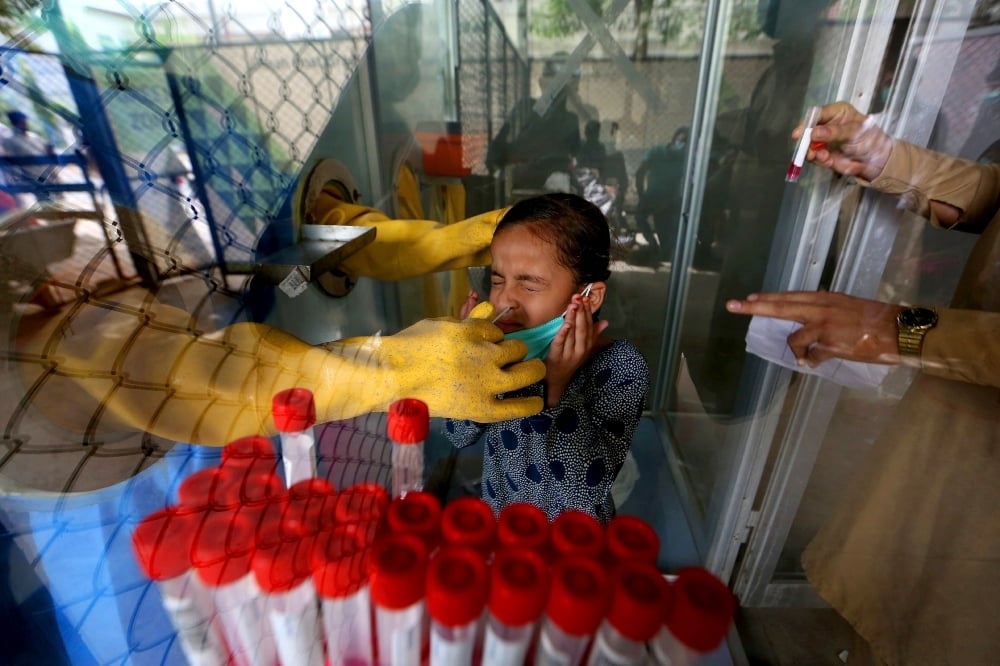 A young girl reacts while having a nasal swab sample taken by a health worker at a Covid-19 testing facility in a hospital in Karachi on March 18. &mdash; AP