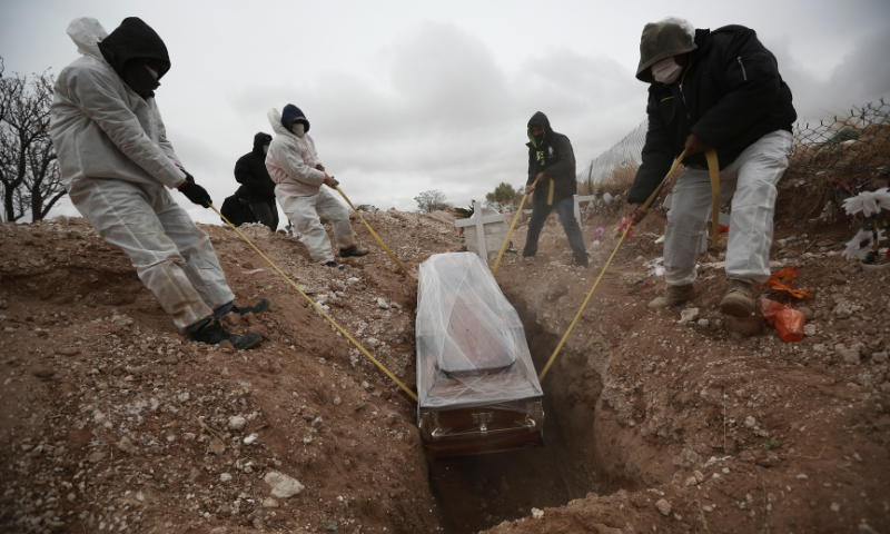 Workers wearing full protection gear lower a coffin into a grave in an area of the San Rafael municipal cemetery in Ciudad Juarez, Mexico. — AP