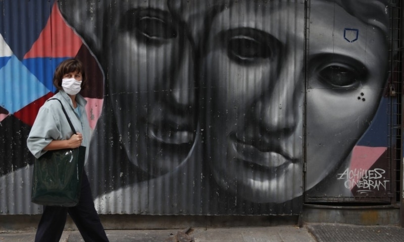 A woman wearing a face mask to protect from the spread of coronavirus, stands in front of a graffiti by the Greek artist Achilles in Athens, Greece, April 6. — AP
