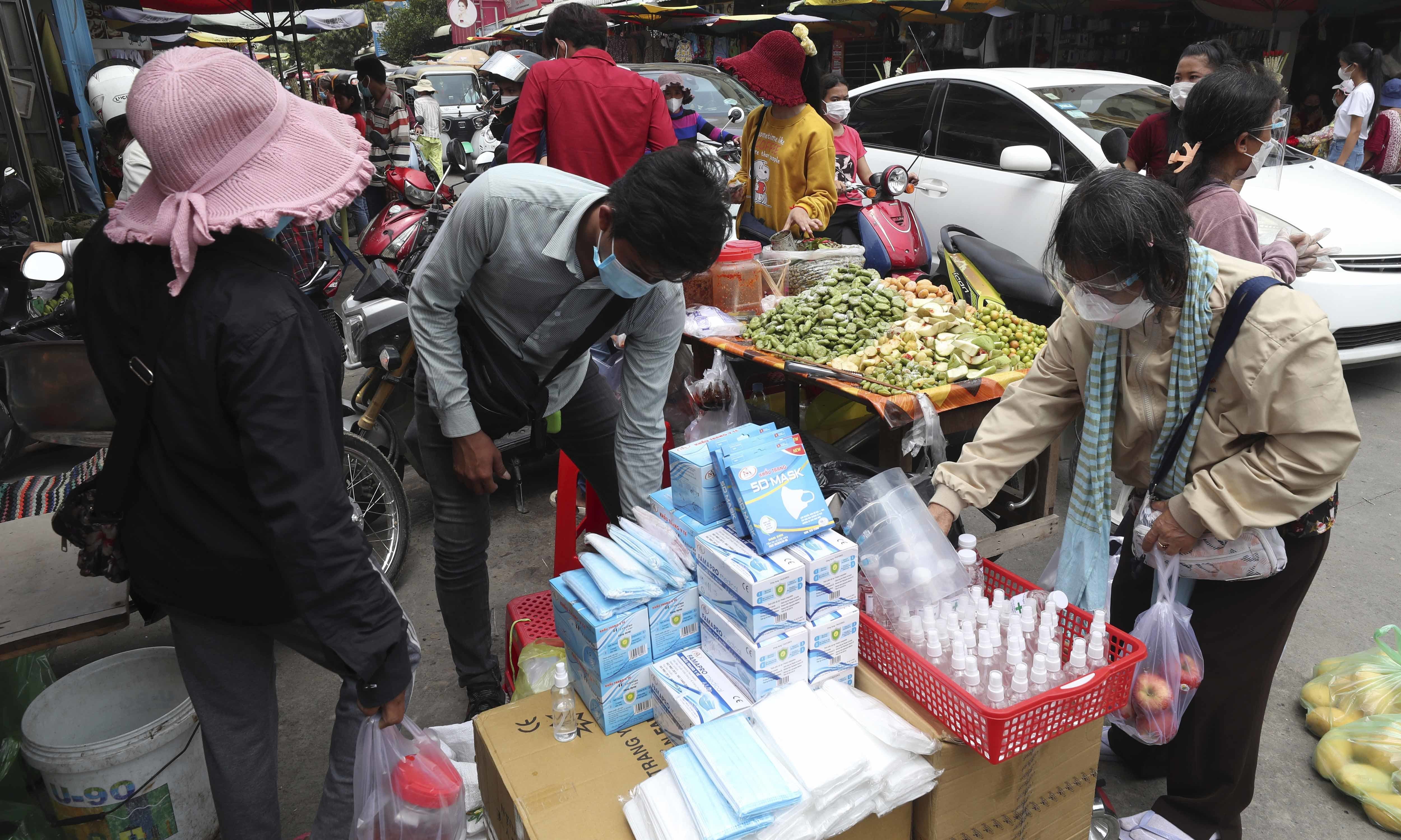 A custome wearing a protective face mask to prevent the spread of the coronavirus buys items at a local market outside Phnom Penh on April 10. &mdash; AP