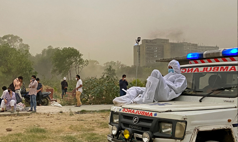 A driver wearing protective gear sits on the bonnet of an ambulance while waiting for the dead body of a Covid-19 victim to be taken for burial at a graveyard in New Delhi. &mdash; AFP