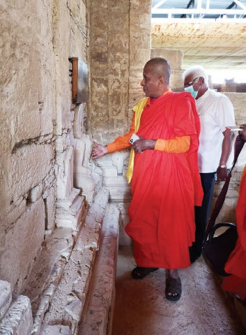 A monk examines a statue at an archaeological site in Khanpur on Thursday. — Dawn