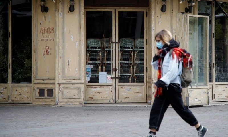A woman, wearing a protective face mask, walks past a closed restaurant in Paris, France, April 29. &mdash; Reuters