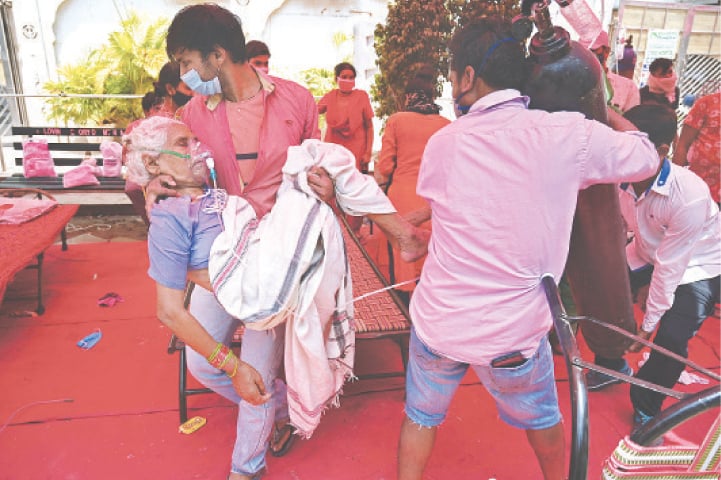 GHAZIABAD: A family member carries a patient breathing with the help of oxygen provided by a Gurdwara under a tent installed along a road.—AFP