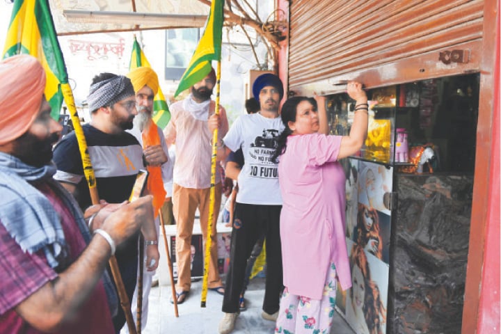 AMRITSAR: Farmers urge a shopkeeper to open her shop as they take part in a protest against the weekend lockdown imposed by the state government as a preventive measure against the spread of Covid-19 on Saturday.—AFP