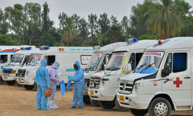 Family members and relatives wearing protective gear stand next to ambulances carrying the bodies of victims who died of Covid-19 at an open-air crematorium on the outskirts of Bangalore. &mdash; AFP