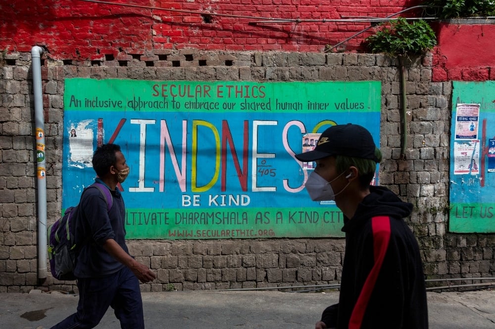 People wearing protective masks walk past a painted wall during a curfew imposed to curb the spread of the coronavirus in Dharmsala on May 15. — AP