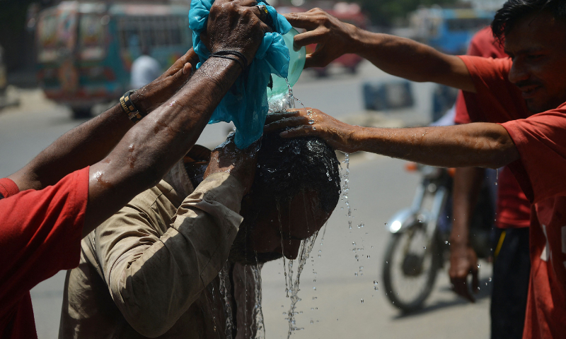 Volunteers from Edhi Foundation cool off a man with water along the roadside in Karachi on Monday. — AFP