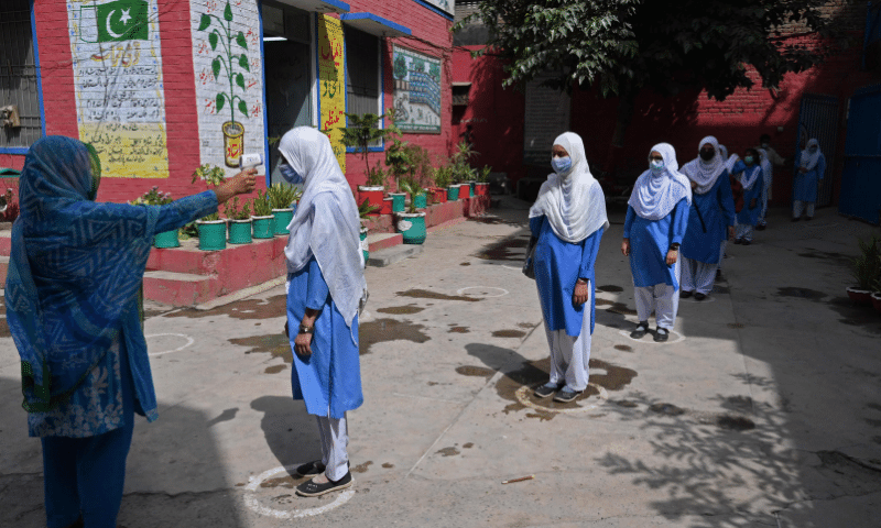A teacher checks the body temperature of a student upon her arrival at a school in Lahore. &mdash; AFP