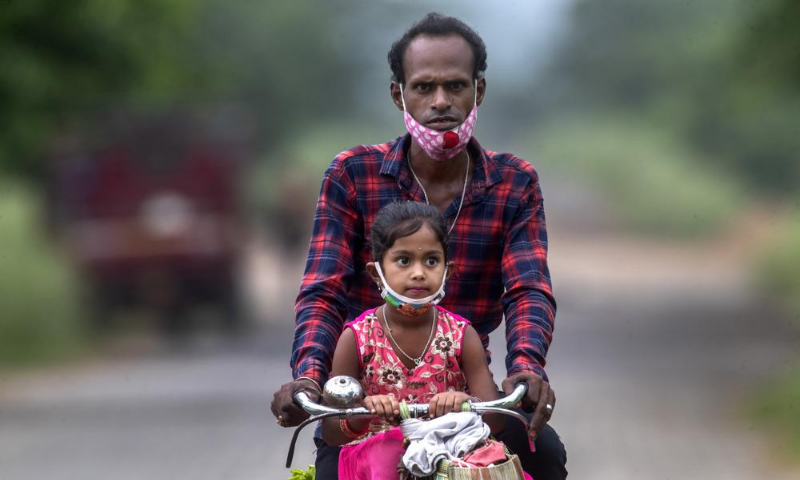 An Indian villager and a child wearing masks on their chins ride on a bicycle on the outskirts of Gauhati, India. — AP