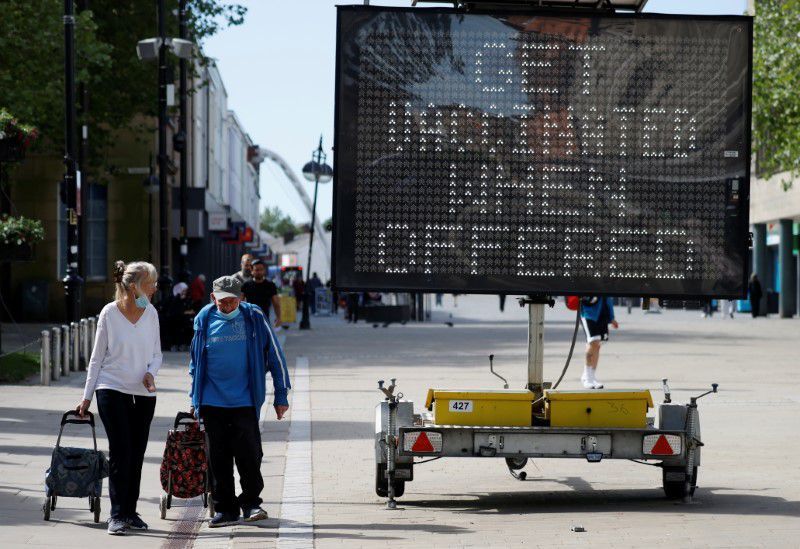 People pull shopping carts as they walk past an information board in Bolton, Britain, June 16. &mdash; Reuters