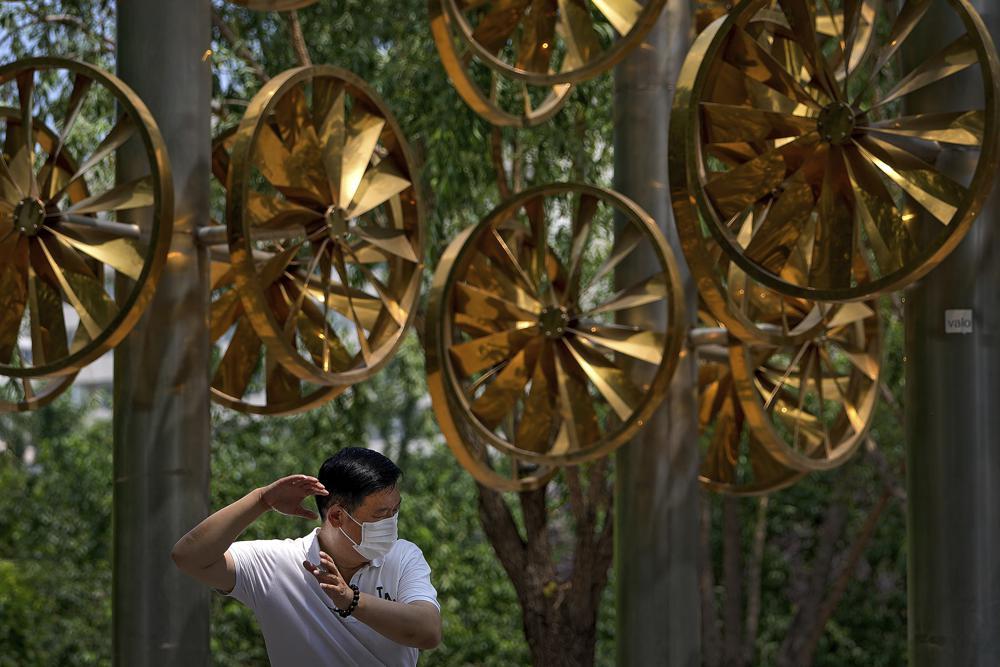 A man wearing a face mask to help protect from the coronavirus exercises near a fan installation at a public park in Beijing, June 15. — AP
